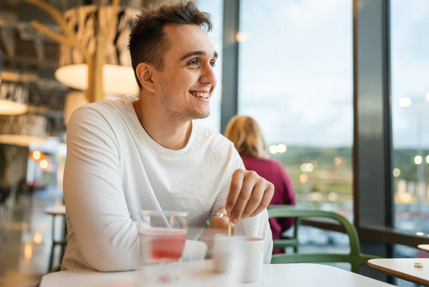 One man young adult Caucasian man sit at cafe or restaurant alone looking to the side having a cup of coffee real people copy space happy smile - Fotoğraf, Görsel