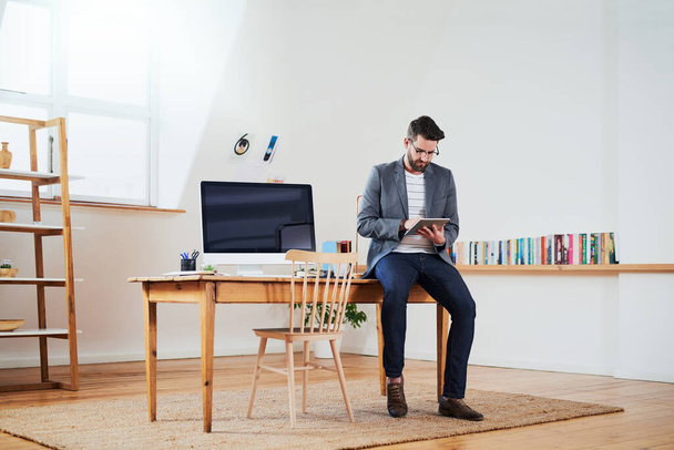 Het hoofdkantoor is klaar voor succes. een knappe jonge zakenman werkt op een tablet terwijl hij in zijn kantoor thuis zit - Foto, afbeelding