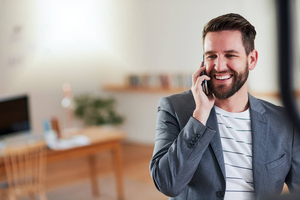 Bedankt voor het terugbellen. een knappe jonge zakenman praten op zijn mobiele telefoon terwijl hij in zijn eigen kantoor - Foto, afbeelding