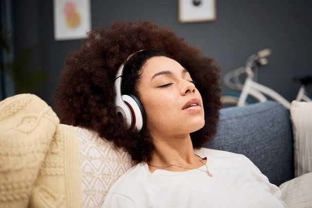 Music, relax and black woman on a sofa listening to radio, streaming or wellness podcast in a living room. Headphones, woman and rest on a couch with online audio track, meditation and playlist. - Foto, Bild