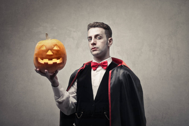 portrait of man disguised as Dracula with a halloween pumpkin in his hand - Valokuva, kuva