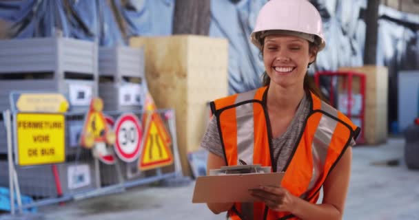 Muotokuva naispuolisesta rakennustyöläisestä kypärässä ja turvaliivi hymyilemässä kameralle työmaalla. Millennial esimies nainen työskentelee. 4 k. - Materiaali, video