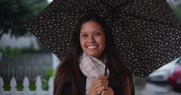 Uśmiechnięta młoda biała kobieta z parasolem na sąsiedniej ulicy, gdy pada deszcz. Szczęśliwa tysiącletnia dziewczyna po dwudziestce w czasie burzy deszczowej na przedmieściach. 4k - Materiał filmowy, wideo