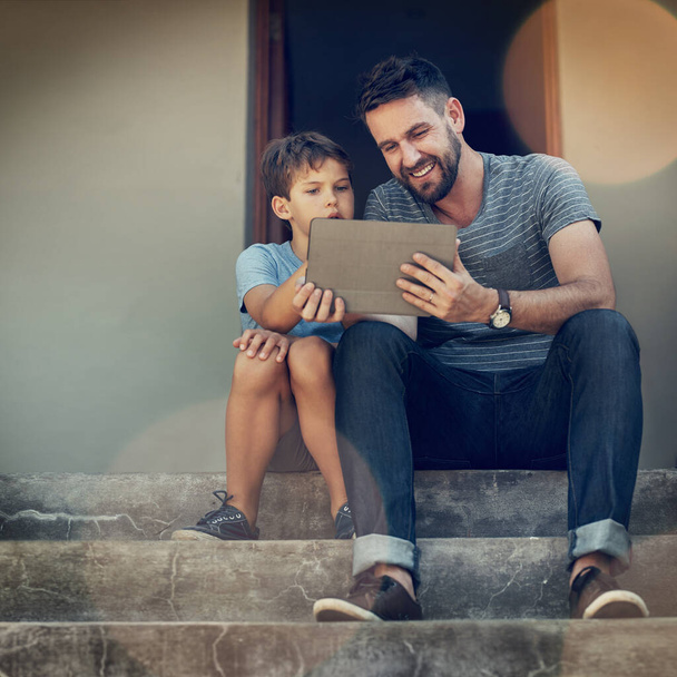 Juste une autre façon dont la technologie encourage le temps de qualité. un père et son fils utilisant une tablette numérique ensemble sur les marches avant de leur maison - Photo, image