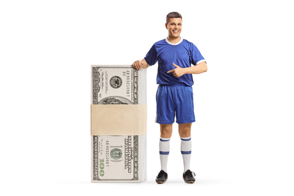 Man in a sports jersey pointing at a stack of money isolated on white background - Photo, Image