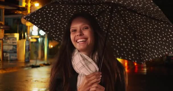 Happy millennial female on city street at night spinning umbrella. Caucasian woman in her 20s standing in the rain and smiling. 4k - Footage, Video