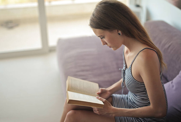 young woman reads a book on the sofa - Foto, Bild