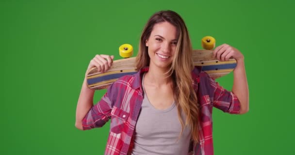 Porträt eines lächelnden Millennialmädchens, das mit Skateboard auf einem grünen Bildschirm posiert. Auf einem grünen Bildschirm, der getastet oder zusammengesetzt werden soll. - Filmmaterial, Video