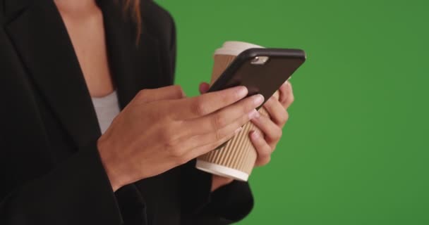 Primer plano de la mujer de negocios utilizando el teléfono inteligente y mensajes de texto mientras sostiene la taza de café en la pantalla verde. Tight shot de mujer profesional que envía mensajes de texto con el teléfono inteligente y la celebración de la taza de beber. 4k - Metraje, vídeo