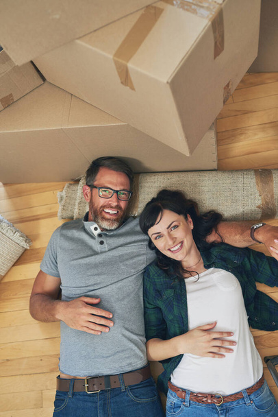 Vettünk egy új házat, jól alakulnak a dolgok. Nagylátószögű portré egy boldog párról, akik együtt pihennek otthonukban a költözés napján. - Fotó, kép