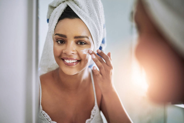 Solo uso los mejores productos para mi piel. Retrato de una joven atractiva que se aplica crema hidratante en la cara en el baño - Foto, imagen