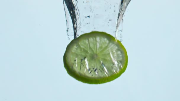 Een stuk citrus dompelen in transparant water met bubbels close-up. Verse limoenschijfje valt diep onder water in super slow motion. Lekker biologisch fruit voor vitamine cocktails heerlijk sap. - Video