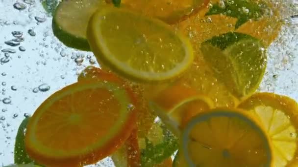 ジューシーな柑橘系の果物は、おいしいレモネードを閉じるためにきれいな水でミントで落ちた。超スローモーションで泡が浮かぶ新鮮なスライスオレンジレモンライム。健康的な生活の中でビタミン食品. - 映像、動画