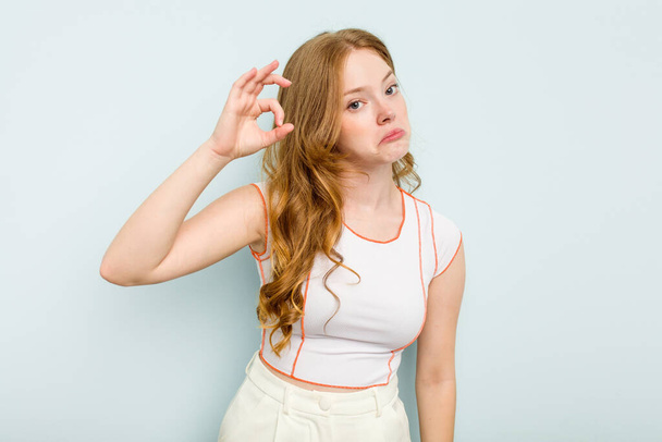 Young caucasian woman isolated on blue background winks an eye and holds an okay gesture with hand. - Photo, image