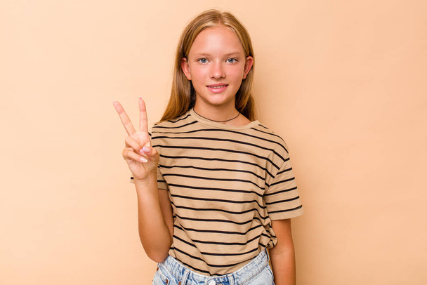 Caucasian teen girl isolated on beige background showing victory sign and smiling broadly. - Foto, immagini
