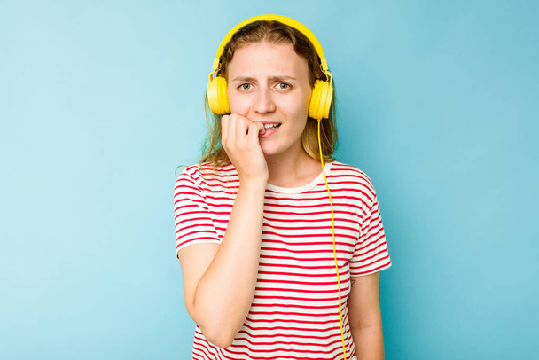 Young caucasian woman wearing headphones isolated on blue background biting fingernails, nervous and very anxious. - Photo, Image