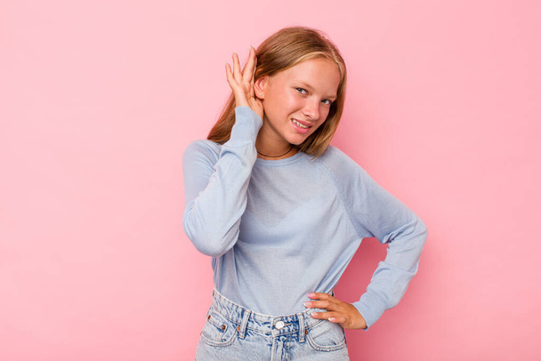 Caucasian teen girl isolated on pink background trying to listening a gossip. - Foto, Imagem