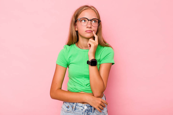 blank tiener meisje geïsoleerd op roze achtergrond overweegt, het plannen van een strategie, na te denken over de manier van een bedrijf. - Foto, afbeelding
