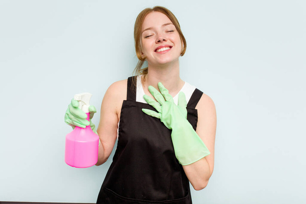 Young cleaner woman isolated on blue background laughs out loudly keeping hand on chest. - Photo, Image