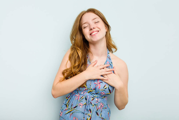 Young caucasian woman isolated on blue background laughing keeping hands on heart, concept of happiness. - Photo, Image
