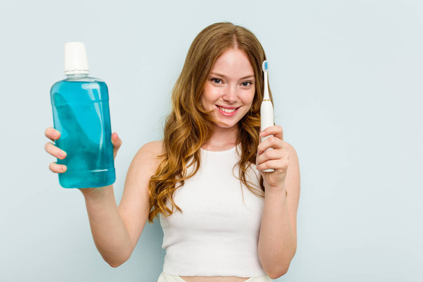 Young caucasian woman holding a mouthwash and toothbrush isolated on blue background - Photo, Image