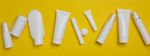 Various types of white plastic packaging: a bottle, a jar, a tube on a yellow background. Container for cosmetics, top view - Photo, Image