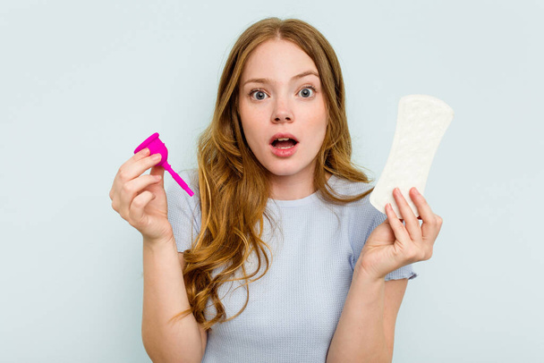 Young caucasian holding menstrual cup and sanitary napkin isolated on blue background - Photo, image