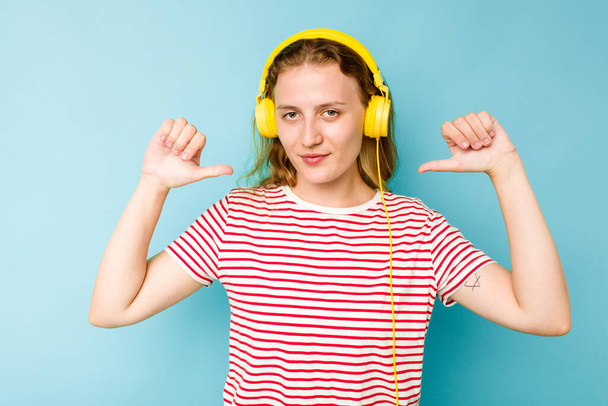 Young caucasian woman wearing headphones isolated on blue background feels proud and self confident, example to follow. - Photo, Image