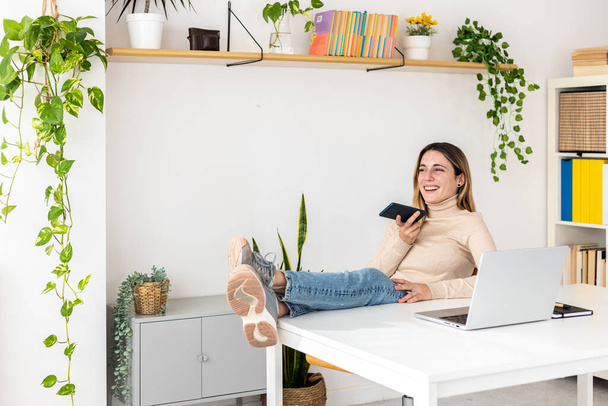 若いビジネス女性が机の上に足で携帯電話を使用してオフィスでリラックス – 技術と起業家の人々の概念 - 写真・画像