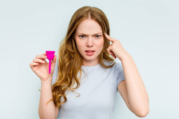 Fiatal kaukázusi nő kezében menstruációs csésze elszigetelt kék háttér mutató csalódottság gesztus mutatva mutatva mutatva mutatóujj. - Fotó, kép