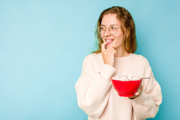 Молода біла жінка тримає тарілку з зерновими, ізольовані на синьому фоні, розслаблено думаючи про щось, дивлячись на простір для копіювання
. - Фото, зображення