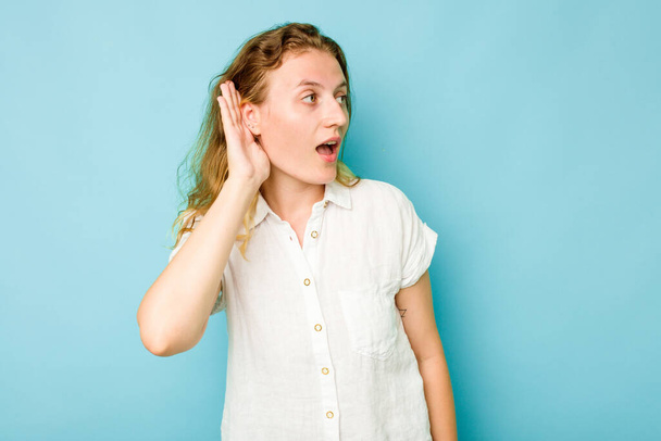 Mladá běloška žena izolované na modrém pozadí se snaží poslouchat klepy. - Fotografie, Obrázek