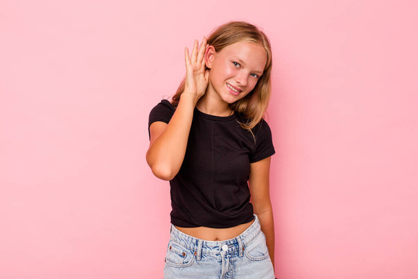 Caucasian teen girl isolated on pink background trying to listening a gossip. - Foto, afbeelding