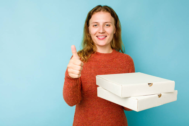 Nuori valkoihoinen nainen tilalla pizzat laatikot eristetty sinisellä taustalla hymyillen ja nostamalla peukalo ylös - Valokuva, kuva