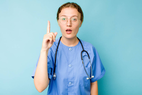 Joven enfermera caucásica aislada sobre fondo azul teniendo alguna gran idea, concepto de creatividad. - Foto, Imagen