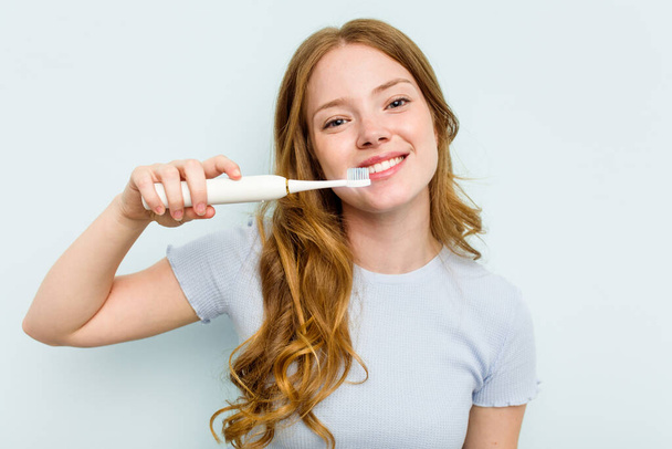 Fiatal fehér nő gazdaság elektromos fogkefe elszigetelt kék háttér - Fotó, kép