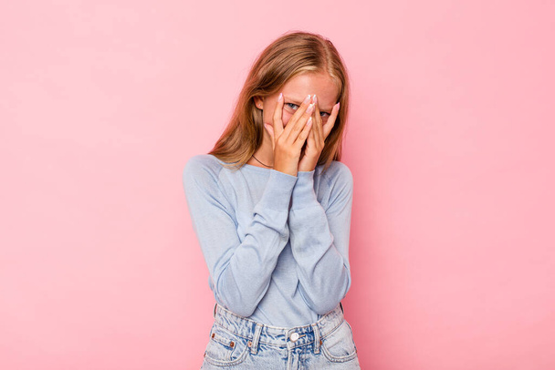 Caucasian teen girl isolated on pink background blink at the camera through fingers, embarrassed covering face. - Foto, imagen