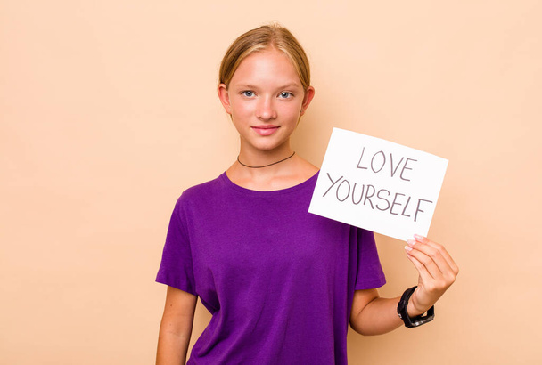 Little caucasian woman holding love yourself placard isolated on beige background - Foto, Imagem