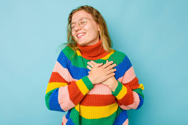 Young caucasian woman isolated on blue background laughing keeping hands on heart, concept of happiness. - Foto, Imagen