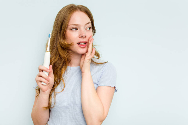 Mavi arka planda elektrikli diş fırçası tutan beyaz bir kadın gizli bir sıcak fren haberinin olduğunu söylüyor. - Fotoğraf, Görsel