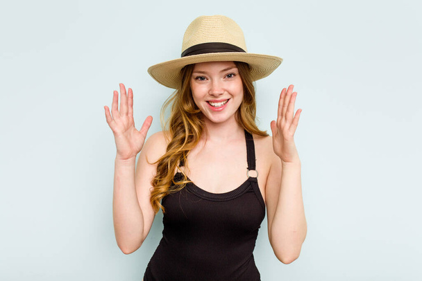 Young caucasian woman going to the beach isolated on blue background receiving a pleasant surprise, excited and raising hands. - Photo, Image
