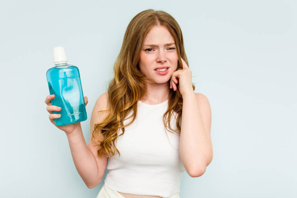 Nuori valkoihoinen nainen, jolla on suuvesi, joka on eristetty sinisellä pohjalla peittäen korvat käsillään. - Valokuva, kuva
