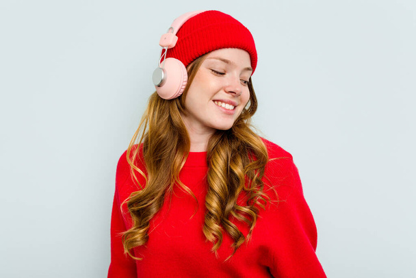Young caucasian woman wearing headphones isolated on blue background - 写真・画像