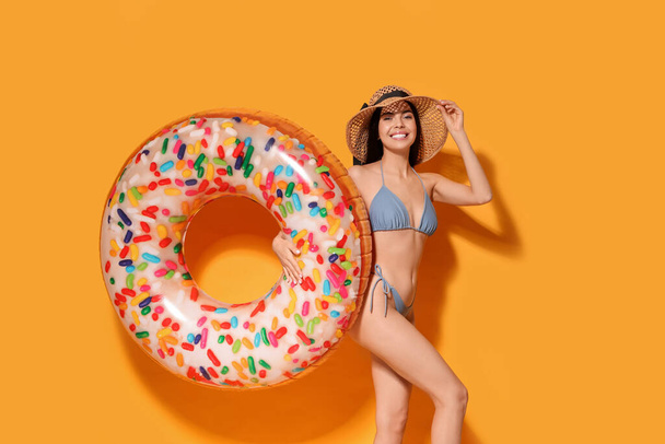 Young woman with straw hat holding inflatable ring against orange background - Foto, Imagen