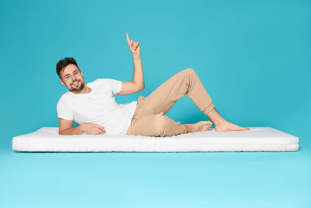 Man on soft mattress pointing upwards against light blue background - Φωτογραφία, εικόνα