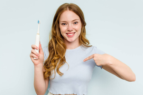 Mavi arka planda elektrikli diş fırçası tutan beyaz bir kadın gömleğin fotokopi odasını işaret ediyor, gururlu ve kendinden emin. - Fotoğraf, Görsel
