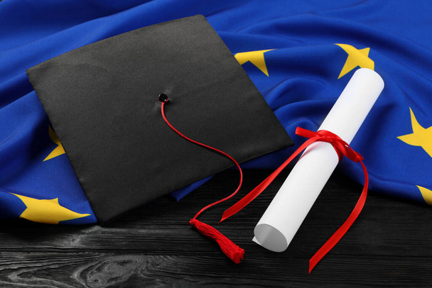 Mezuniyet şapkası, diploma ve Avrupa Birliği bayrağı siyah ahşap masa üzerinde - Fotoğraf, Görsel