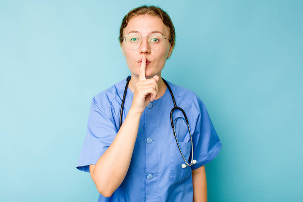 Νεαρή νοσοκόμα καυκάσια γυναίκα απομονωμένη σε μπλε φόντο κρατώντας ένα μυστικό ή ζητώντας σιωπή. - Φωτογραφία, εικόνα