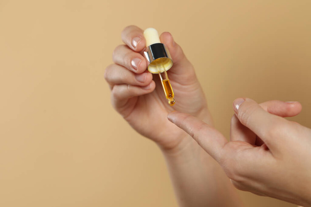 Young woman applying essential oil onto finger on beige background, closeup. Space for text - 写真・画像