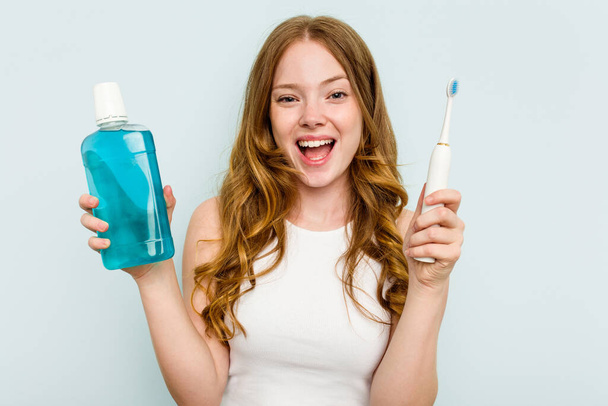 Młoda biała kobieta trzymająca płyn do płukania jamy ustnej i szczoteczkę do zębów na niebieskim tle - Zdjęcie, obraz